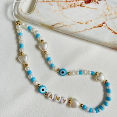 a blue and white beaded necklace with an evil eye on it, next to a cell phone