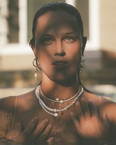 a woman wearing pearls and necklaces standing in water with her hands on her chest