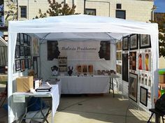 a white tent with pictures on the wall and tables under it in front of a building