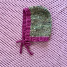 a knitted hat is laying on top of a pink sweater with a green patch