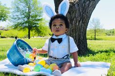 a little boy dressed up in bunny ears sitting on a blanket with an easter basket