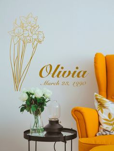 a yellow chair and table with flowers on it in front of a wall decal