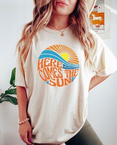 Here Comes the Sun T Shirt, Sunshine Shirt, Summer T-shirt, Travel Beach Vacation Shirt, Camping Shirt, Hippie T-Shirt, Motivational T-Shirt Thank you for shopping with us❤️ Size - Our products are unisex fit - You can check our size and color charts on our listing photos. How To Order - Select a size - Select a t-shirt color - If available, indicate the design (text) color in the personalization box - Click add to cart. You can go back to add more shirts. - Click "Proceed to check out". Brands Retro Cotton T-shirt For Beach, Retro Text Print T-shirt For Beach, Beach Cotton T-shirt With Front Print, Beach Cotton T-shirt With Slogan, Pre-shrunk Graphic Tee For Beach Season, Retro Cotton T-shirt For The Beach, Beach T-shirt With Front Print And Crew Neck, Retro Letter Print T-shirt For Beach Season, Summer Crew Neck Top With Text Print