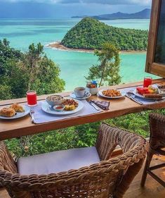 an outdoor table with plates of food and drinks on it overlooking the ocean in front of a tv