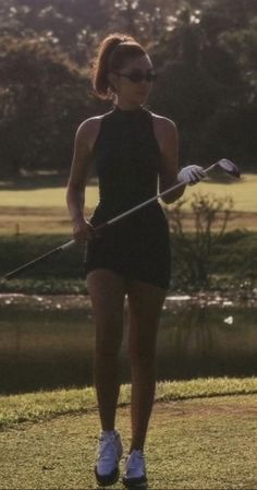 a woman holding a golf club on top of a field