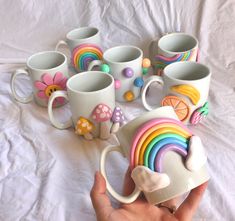 a hand holding a coffee cup with many different designs on it and several mugs in the shape of rainbows