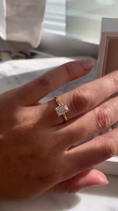 a woman's hand holding an engagement ring in front of a box on a table