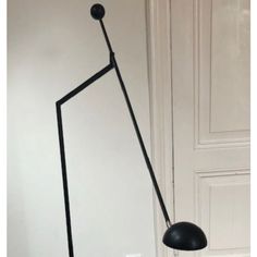 a black floor lamp sitting on top of a white wall next to a doorway with a door in the background