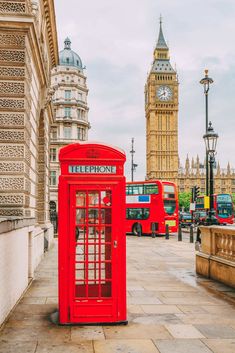 a red phone booth sitting on the side of a street next to a clock tower