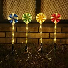 three colorful lights sitting on top of grass next to a brick wall in the dark