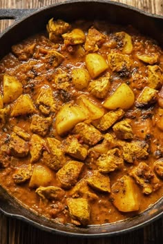 a pan filled with curry and potatoes on top of a wooden table