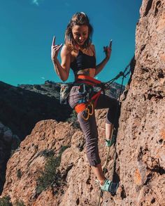 a woman climbing up the side of a mountain with her hands in the air while holding on to ropes