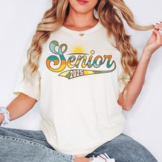 a woman sitting on the floor with her legs crossed and wearing a white shirt that says senior