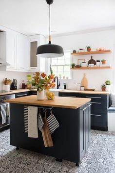 a kitchen with black cabinets and wooden counter tops, an island in front of the stove