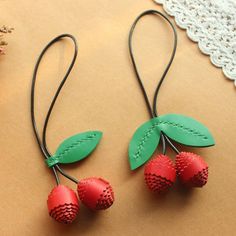 two red cherries with green leaves are hanging from leather cord on a lace doily