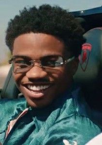 a man with glasses sitting in the back seat of a car smiling at the camera