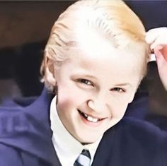 a young boy wearing a suit and tie smiling at the camera with his hand on his head