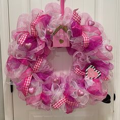 a pink and white wreath hanging on the front door with a bird decoration attached to it