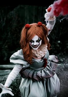 a creepy doll dressed in white with red hair and makeup, holding her arms out