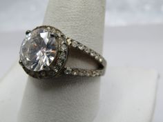 Vintage Sterling CZ Rhinestone Ring, Sz. 10.5.  The main stone is clear with nice sparkle and is appx. 10mm round.  It is set with four prongs.  It has a halo of 1mm clear rhinestones that also goes half way  down in the band in an open v split band.  The band is appx. 8mm wide and tapers to 2.5mm at the back of the finger.  This tests as sterling and is marked sterling with an appx weight of 9.12 gr.  Very good condition other than oxidation that will polish away.  It is not signed by the maker.  Age is estimated at 1980's-1990's.  (W121722.1X1 Ss9477 J LD 2/5/23) (JK 6.9.2024) You can search me at my own store: mariasvintage.com and also I have an etsy store at mariasvintage2.com or on pinterest under pinterest.com/mariasvinta0654/ where I have most of my items for sale across all my ven Dazzling Halo Ring With Prong Setting And Round Stone, Dazzling Round Halo Ring, Sparkling Crystal Ring For Wedding, Sparkling Crystal Wedding Ring, Diamond Bling Promise Ring, Cubic Zirconia Halo Ring With Prong Setting, Party Rings With Bling, Silver Halo Ring With Center Round Stone, Silver Halo Ring With Center Stone And Round Stone