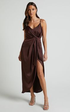 a woman wearing a brown dress with a slit down the side and one leg in front