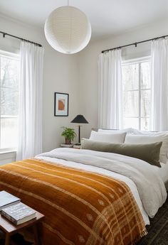 a bedroom with a bed, two windows and a lamp hanging from the ceiling above it