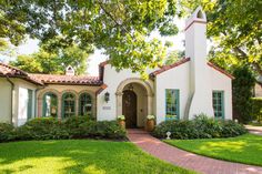 a white house with green shutters on the front and side windows, surrounded by lush greenery