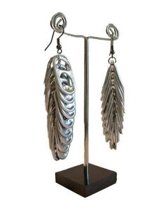 the earrings are made out of metal and have long, wavy leaves hanging from them