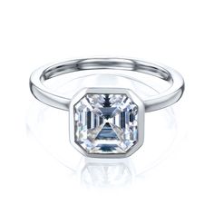 a white gold ring with an emerald cut diamond in the center, on a reflective surface