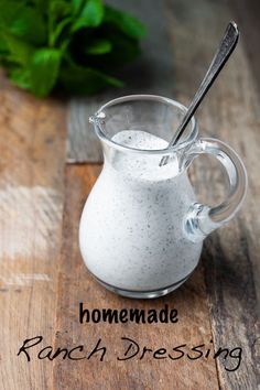 homemade ranch dressing in a glass pitcher on a wooden table with basil leaves behind it