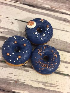 three donuts with blue icing and sprinkles sitting on a wooden table