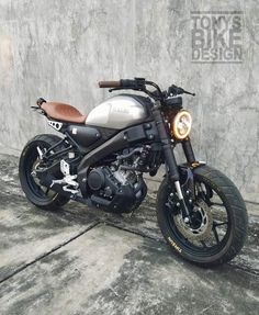 a silver and black motorcycle parked next to a concrete wall with a brown leather seat