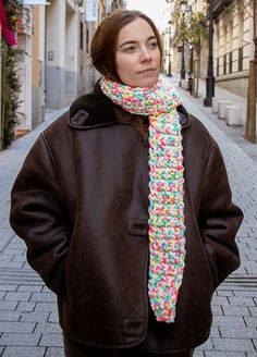 a woman is standing on the street wearing a colorful knitted scarf with sprinkles