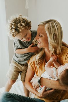 a woman holding a baby while sitting on top of a bed next to a man