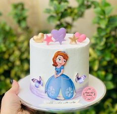 a hand holding a cake decorated with princesses and stars on it's side