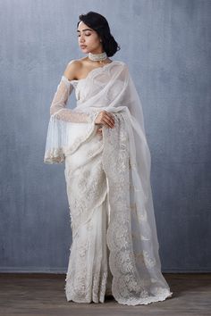 a woman wearing a white sari with sheer sleeves and lace on the top, standing in