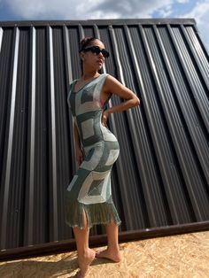 a woman standing in front of a building wearing sunglasses and a dress with fringes