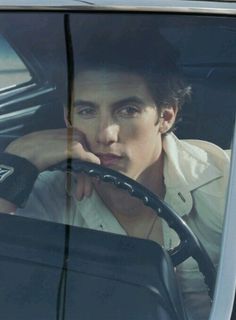 a man sitting in the driver's seat of a car with his hand on the steering wheel