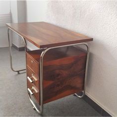 a wooden desk with metal legs and drawers on the bottom, next to a white wall