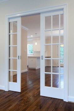 an empty living room with wood floors and white doors that lead into the kitchen area