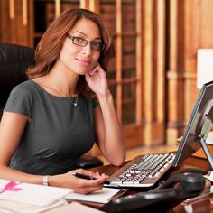 a woman sitting at a desk with a laptop computer in front of her, smiling