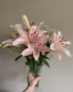 a vase filled with pink lilies and baby's breath in someones hand