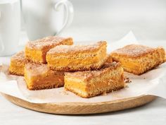 several pieces of cake sitting on top of a wooden plate next to a cup and saucer