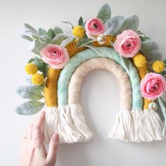 a person holding up a wall decoration with flowers and fringes on the front of it