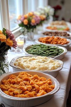 several dishes of food are lined up on a table with flowers in the vases