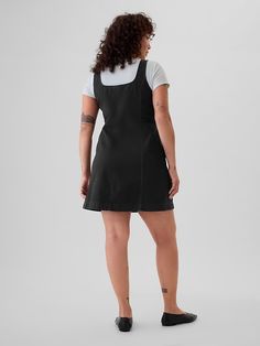 a woman wearing an apron dress and black slip - ons is looking back at the camera