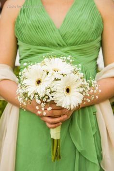 a woman in a green dress holding a bouquet of daisies and baby's breath