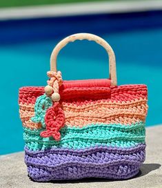 a colorful crocheted purse sitting on top of a cement wall next to a swimming pool