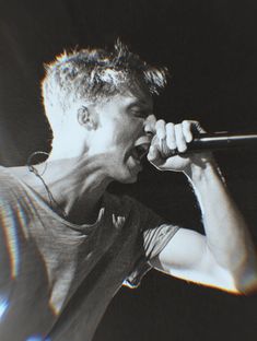 a man singing into a microphone while holding it in his right hand and wearing a t - shirt