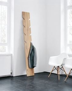 two chairs and a coat rack in a room with white walls, black flooring and windows